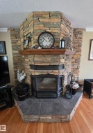 Corner stone fireplace with a wood mantel, slate tile hearth, and wood-finish flooring - 