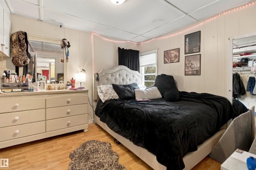 Bright bedroom featuring a tufted upholstered bed frame, wood-finish flooring, a ceiling-mounted light fixture, and ample natural light from multiple windows - 12707 73 Street Nw, Edmonton, AB 