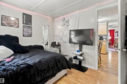 Spacious bedroom with wood-finish flooring, accent wall with artistic mural, and built-in media console with mounted flat-screen television - 