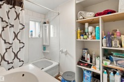 Bathroom featuring a spacious walk-in shower with geometric patterned curtain, pedestal sink, and extensive built-in cabinetry with wood-finish shelving - 