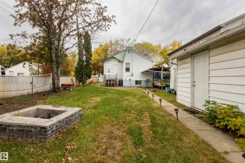 Expansive backyard featuring a built-in fire pit with brick detailing, mature trees, and a concrete pathway with pathway lighting - 12707 73 Street Nw, Edmonton, AB 