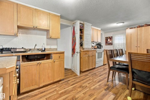 Wood-finish flooring throughout, light wood-tone cabinetry, white subway tile backsplash, recessed shelving, and a dining area - 12707 73 Street Nw, Edmonton, AB 