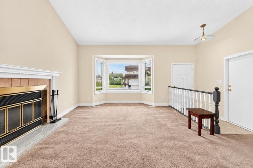 Vaulted ceiling, bay window, tiled fireplace with gold-toned insert, neutral carpeting, and white painted railing - 7307 152C Avenue Nw, Edmonton, AB 