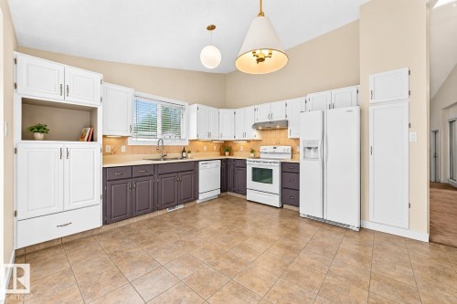 Kitchen with tile flooring, white cabinetry, contrasting lower cabinetry, and a full suite of white appliances - 7307 152C Avenue Nw, Edmonton, AB 