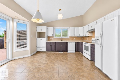 Kitchen featuring white appliances, a vaulted ceiling, recessed lighting, and a sliding glass door to an outdoor deck - 7307 152C Avenue Nw, Edmonton, AB 