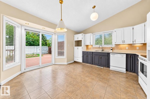 Kitchen with two-tone cabinetry, a sliding glass door, and tiled flooring - 7307 152C Avenue Nw, Edmonton, AB 