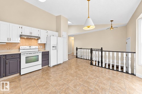Kitchen featuring white upper cabinetry, dark lower cabinetry, tiled backsplash, and tile flooring - 7307 152C Avenue Nw, Edmonton, AB 