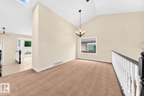 Vaulted ceiling with a skylight, carpeted flooring, chandelier, and white railing with a dark top rail - 7307 152C Avenue Nw, Edmonton, AB 