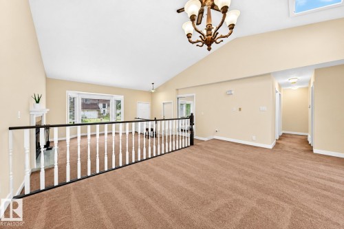 Vaulted ceiling with a skylight, chandelier lighting, wall-to-wall carpeting, and a white wood-spindle railing - 7307 152C Avenue Nw, Edmonton, AB 