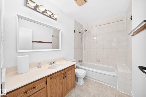 Bathroom featuring a single vanity with wood-finish cabinetry and an integrated sink, a large framed mirror, and a tiled shower/tub combination - 7307 152C Avenue Nw, Edmonton, AB 