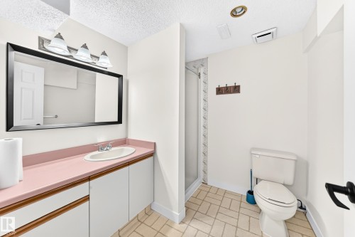 Bathroom featuring an elongated vanity with an integrated sink, a rectangular framed mirror, three-light vanity fixture, a toilet, and a shower enclosure - 7307 152C Avenue Nw, Edmonton, AB 