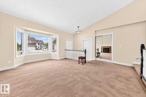 Vaulted ceiling with an attached light fixture, a bay window with integrated blinds, mirrored closet doors, and light-toned carpeting - 7307 152C Avenue Nw, Edmonton, AB 