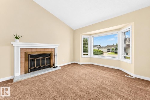 Vaulted ceiling, bay window, carpet flooring, fireplace with white mantel, and a tiled hearth - 7307 152C Avenue Nw, Edmonton, AB 