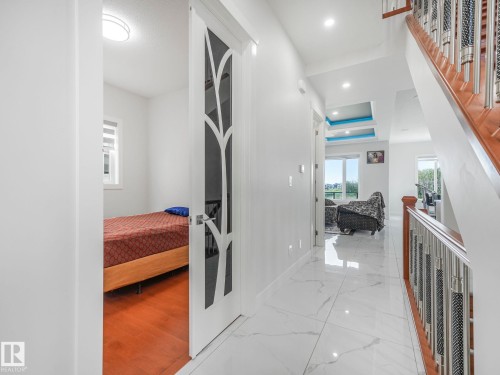 Hardwood flooring in a private room, white hallway with large format tile flooring, recessed lighting, and a wood staircase with metal balusters - 120 38 Street Sw, Edmonton, AB 