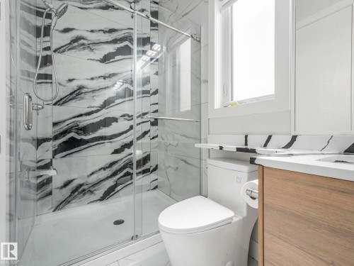 Glass-enclosed shower with black and white patterned tile, sleek shower fixtures, and a white shower base - 120 38 Street Sw, Edmonton, AB 