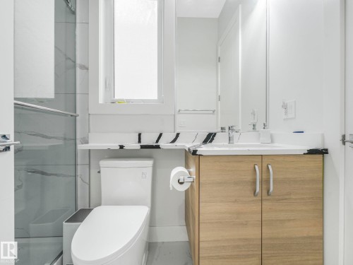 Tiled shower with glass enclosure, wood-finish vanity with countertop, integrated sink, and wall-mounted mirror - 120 38 Street Sw, Edmonton, AB 