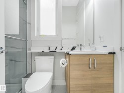 Tiled shower with glass enclosure, wood-finish vanity with countertop, integrated sink, and wall-mounted mirror - 