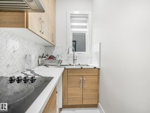 Modern kitchen featuring wood-finish cabinetry, a white countertop, herringbone tile backsplash, and stainless steel appliances - 120 38 Street Sw, Edmonton, AB 