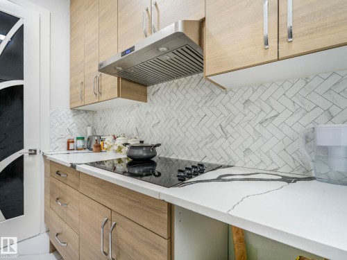 Wood-finish cabinetry with stainless steel hardware, herringbone tile backsplash, integrated cooktop, and light-toned countertops - 120 38 Street Sw, Edmonton, AB 