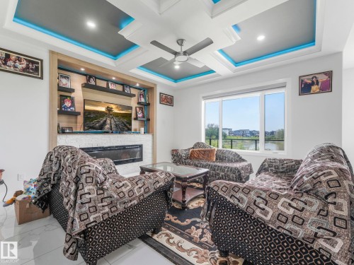 Coffered ceiling with recessed lighting and blue accent illumination, built-in media center with a linear fireplace, wall-mounted shelving, and large windows - 120 38 Street Sw, Edmonton, AB 
