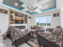 Coffered ceiling with recessed lighting and blue accent illumination, built-in media center with a linear fireplace, wall-mounted shelving, and large windows - 