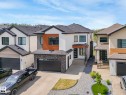 Contemporary architecture featuring a two-car garage, stone and wood exterior accents, multiple windows, a stone-clad entry pillar, and a front walkway - 120 38 Street Sw, Edmonton, AB 