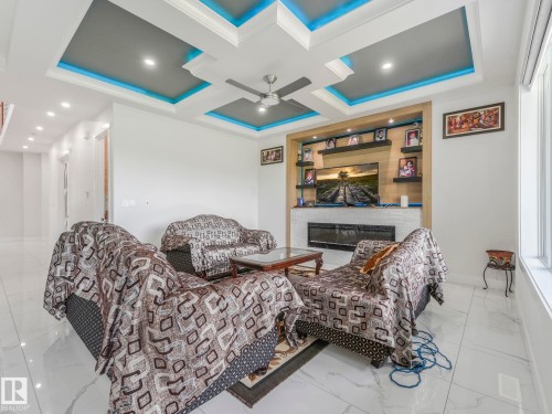 Coffered ceiling with recessed lighting and accent illumination, built-in media console with shelving, integrated electric fireplace, large window with roller shade, and polished tile flooring - 120 38 Street Sw, Edmonton, AB 
