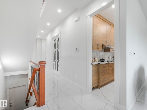 White tile flooring with subtle veining, recessed lighting, and a wood-finish staircase railing - 120 38 Street Sw, Edmonton, AB 