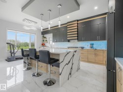 Modern kitchen featuring a large center island with waterfall countertop, recessed ceiling details, pendant lighting, built-in cabinetry, and tile flooring - 