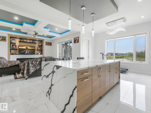 Waterfall island with stone-finish countertop, wood-finish cabinetry, and contemporary pendant lighting - 120 38 Street Sw, Edmonton, AB 