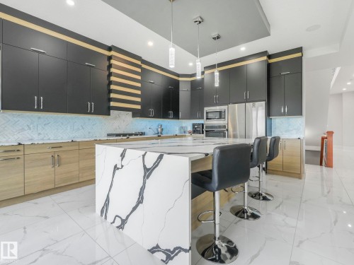 Kitchen featuring a large island with waterfall countertop, stainless steel appliances, two-tone cabinetry, herringbone tile backsplash, and recessed lighting - 120 38 Street Sw, Edmonton, AB 