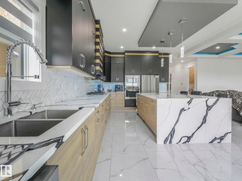 Modern kitchen featuring a large waterfall island with veined stone, stainless steel appliances, and a dual basin sink with a gooseneck faucet - 120 38 Street Sw, Edmonton, AB 