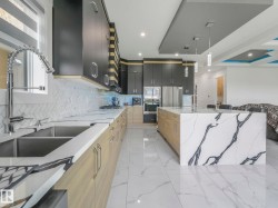 Modern kitchen featuring a large waterfall island with veined stone, stainless steel appliances, and a dual basin sink with a gooseneck faucet - 