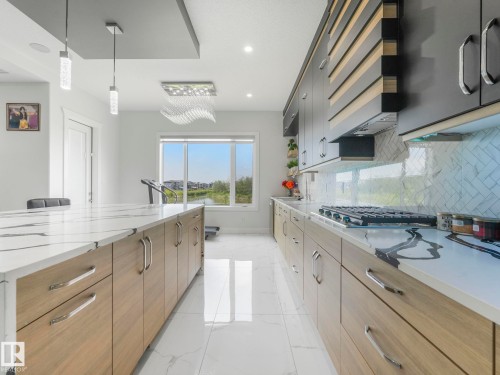 Contemporary kitchen featuring white tile flooring, light wood-finish lower cabinetry, dark upper cabinetry with wood accents, and a white countertop with grey veining - 120 38 Street Sw, Edmonton, AB 