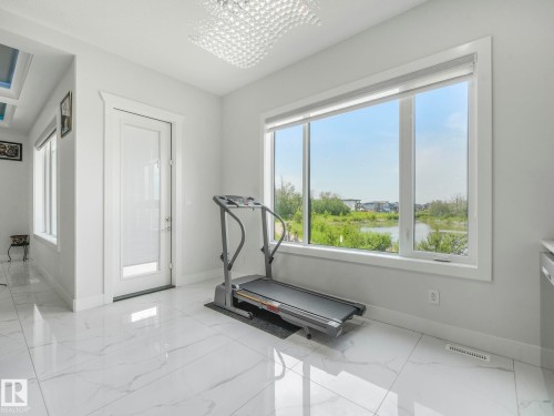 Oversized window with water scenery, white tile flooring, contemporary chandelier, and a glass-paneled door - 120 38 Street Sw, Edmonton, AB 