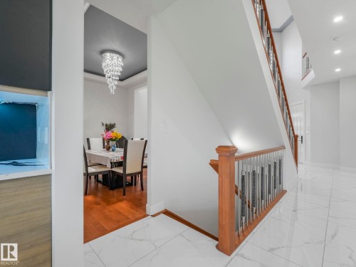 Hardwood flooring in dining area, white tile flooring, wood and metal staircase railing, recessed lighting, and a crystal chandelier - 120 38 Street Sw, Edmonton, AB 