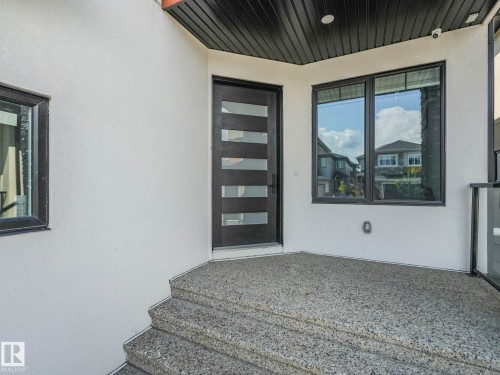 Front entry with a modern black door featuring horizontal glass panels, dark-trimmed windows, and a textured aggregate concrete porch and steps - 120 38 Street Sw, Edmonton, AB 