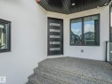 Front entry with a modern black door featuring horizontal glass panels, dark-trimmed windows, and a textured aggregate concrete porch and steps - 120 38 Street Sw, Edmonton, AB 