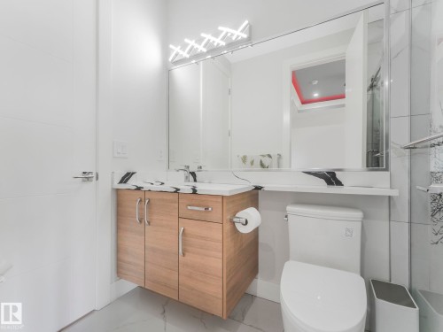 Floating wood-finish vanity with a white countertop, under-mount sink, and contemporary wall-mounted lighting - 120 38 Street Sw, Edmonton, AB 