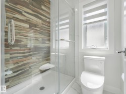 Glass-enclosed shower with decorative wall tiling, white shower pan, and chrome fixtures - 