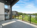 Covered balcony with glass panel railing and textured flooring, overlooking a natural water feature and walking path - 120 38 Street Sw, Edmonton, AB 