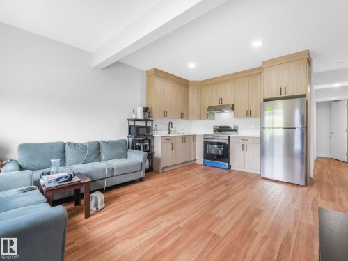 Wood-finish flooring throughout, kitchen with light wood-finish cabinetry, stainless steel appliances, white subway tile backsplash, and recessed lighting - 120 38 Street Sw, Edmonton, AB 
