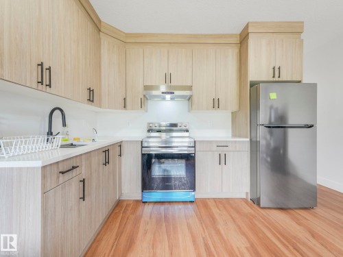 Kitchen featuring wood-finish cabinetry, stainless steel appliances, a black gooseneck faucet, light-toned countertops, and wood-finish flooring - 120 38 Street Sw, Edmonton, AB 