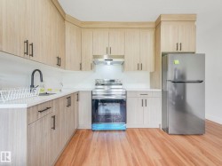 Kitchen featuring wood-finish cabinetry, stainless steel appliances, a black gooseneck faucet, light-toned countertops, and wood-finish flooring - 