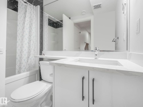 White vanity with a built-in sink and stone-finish countertop, chrome faucet, and dark cabinet hardware - 120 38 Street Sw, Edmonton, AB 