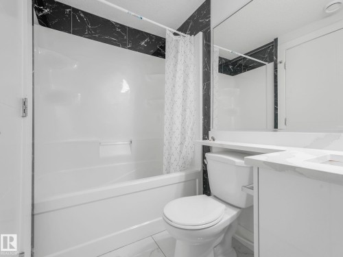 Contemporary bathroom featuring a white bathtub and shower surround, black marble-look wall tiles, a white vanity with an integrated sink, and a large wall-mounted mirror - 120 38 Street Sw, Edmonton, AB 