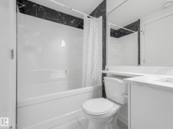 Contemporary bathroom featuring a white bathtub and shower surround, black marble-look wall tiles, a white vanity with an integrated sink, and a large wall-mounted mirror - 