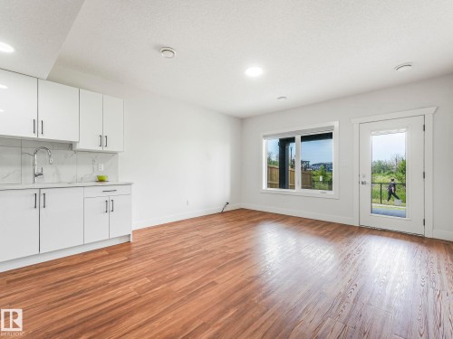 Wood-finish flooring, white cabinetry, integrated sink with gooseneck faucet, backsplash, and glass-paneled exterior door - 120 38 Street Sw, Edmonton, AB 
