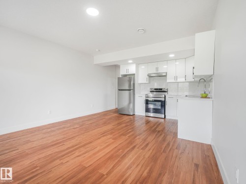 Open-concept living space with wood-finish flooring, recessed lighting, white cabinetry, stainless steel appliances, and a tile backsplash - 120 38 Street Sw, Edmonton, AB 