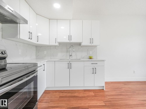 Contemporary kitchen featuring white cabinetry, a stainless steel range hood, white countertops, a white tile backsplash, and wood-finish flooring - 120 38 Street Sw, Edmonton, AB 